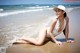 A woman in a white bathing suit and hat laying on the beach.