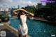 A woman in a white dress standing next to a swimming pool.