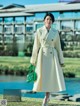 A woman in a white coat is walking by a lake.