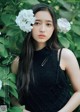 A woman in a black dress standing in front of white flowers.