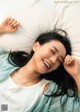 A woman laying in bed with her eyes closed and smiling.