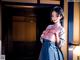 A woman in a blue and pink kimono standing in front of a door.