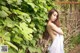 A woman in a white dress standing in front of a bush.